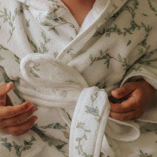 Close-up of a person wearing a white bathrobe with green floral patterns.