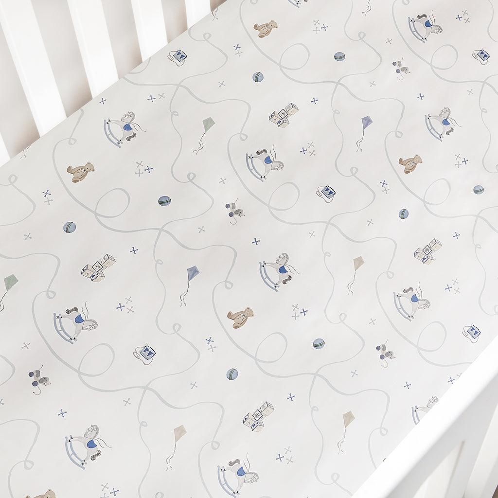 Baby crib sheet with teddy bear and toy horse pattern on a white crib