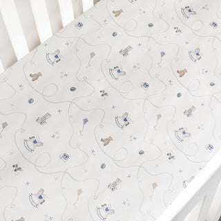 Baby crib sheet with teddy bear and toy horse pattern on a white crib