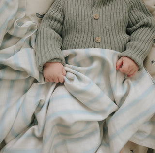 Seaside Stripes Swaddle Blanket in Blue wrapped around baby in bassinet