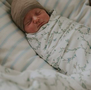 Secret Garden Swaddle in Ivory wrapped around baby in bassinet