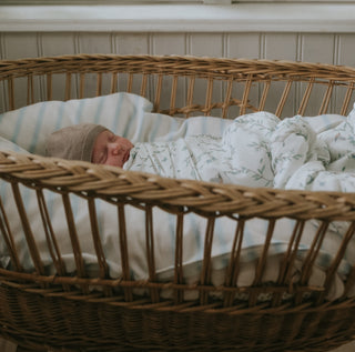 Secret Garden Swaddle in Ivory wrapped around baby in bassinet