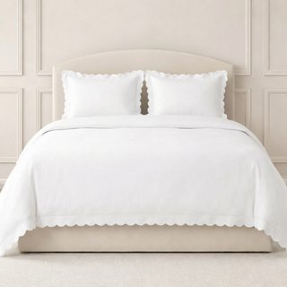 White bedding set with scalloped edges on a bed against a beige wall.