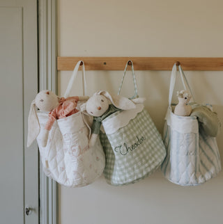Three quilted bags with stuffed animals hanging on a wooden rod against a white wall.