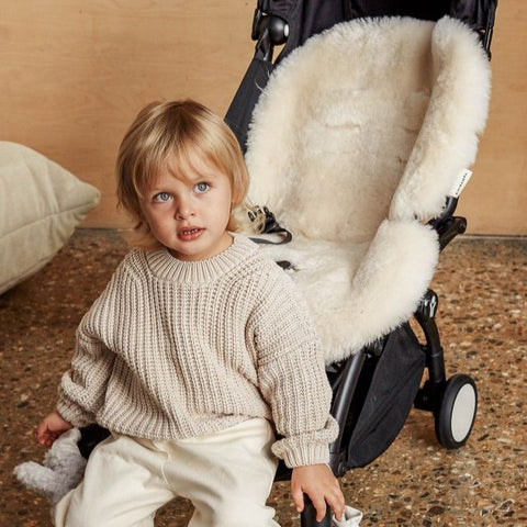Child sitting next to a stroller with a snuggler