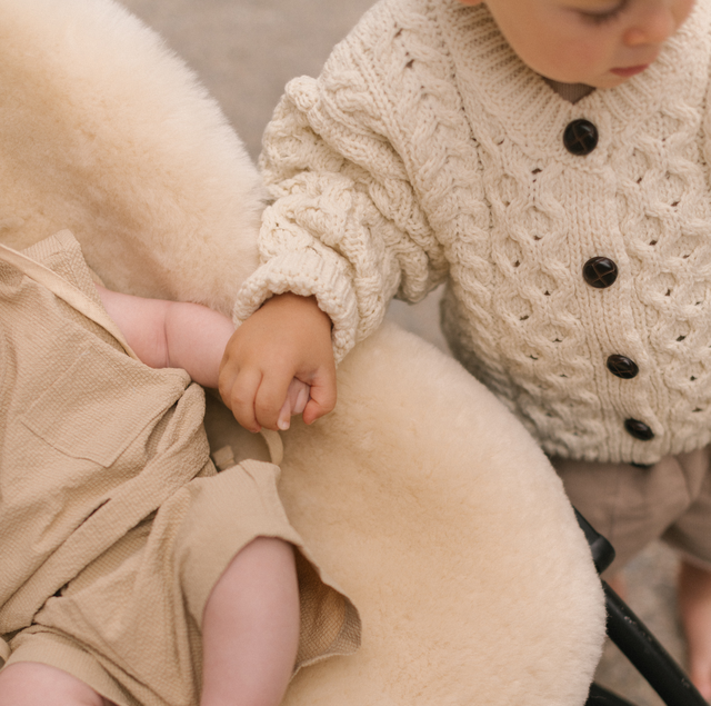 Two children holding hands, one in a textured sweater and the other in a snuggler in stroller