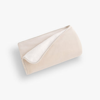 Folded beige blanket with white lining on a light gray background
