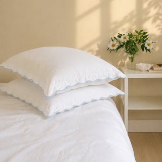 White euro pillows with blue trim on a bed in a softly lit room.