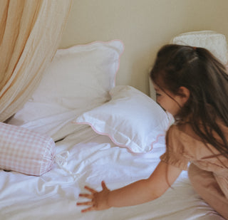 Child playing on a bed with white pillows and light-colored curtains.