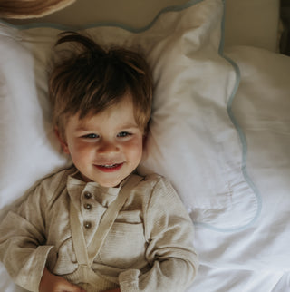 Child lying on a bed with white toddler pillow with blue trim 