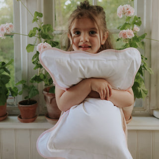 Young girl holding a large white pillow in a room with plants