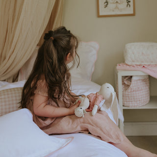 Young girl sitting on a bed holding stuffed animals in a cozy bedroom.