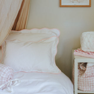 Pink and white bedding with a nightstand in a bedroom setting