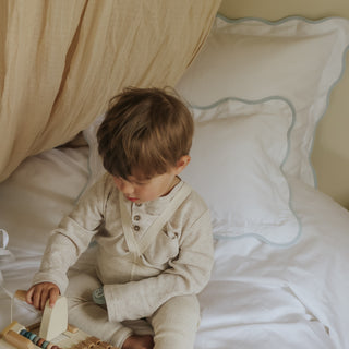 Child playing with a wooden toy on a bed with white bedding with blue trim detail
