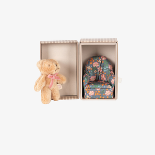 Small teddy bear and floral-patterned chair in an open box on a white background