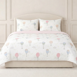 Bed with pastel balloon patterned bedding and pillows against a neutral wall.