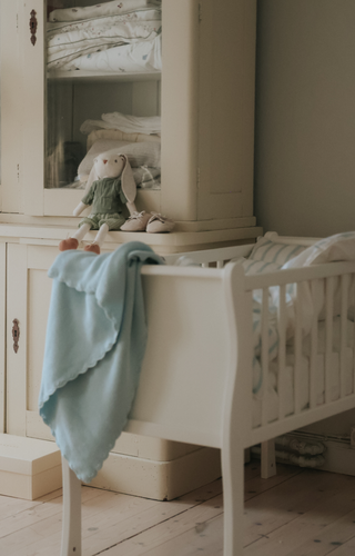 White crib with a light blue blanket in a nursery setting.