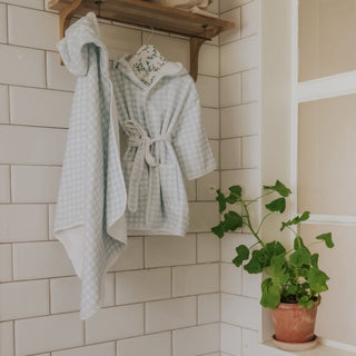 Bathrobes hanging on a rack against a tiled wall with a plant in the corner.