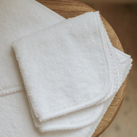Classic washcloth in white with pink trim detail. Folded on top of bath towel