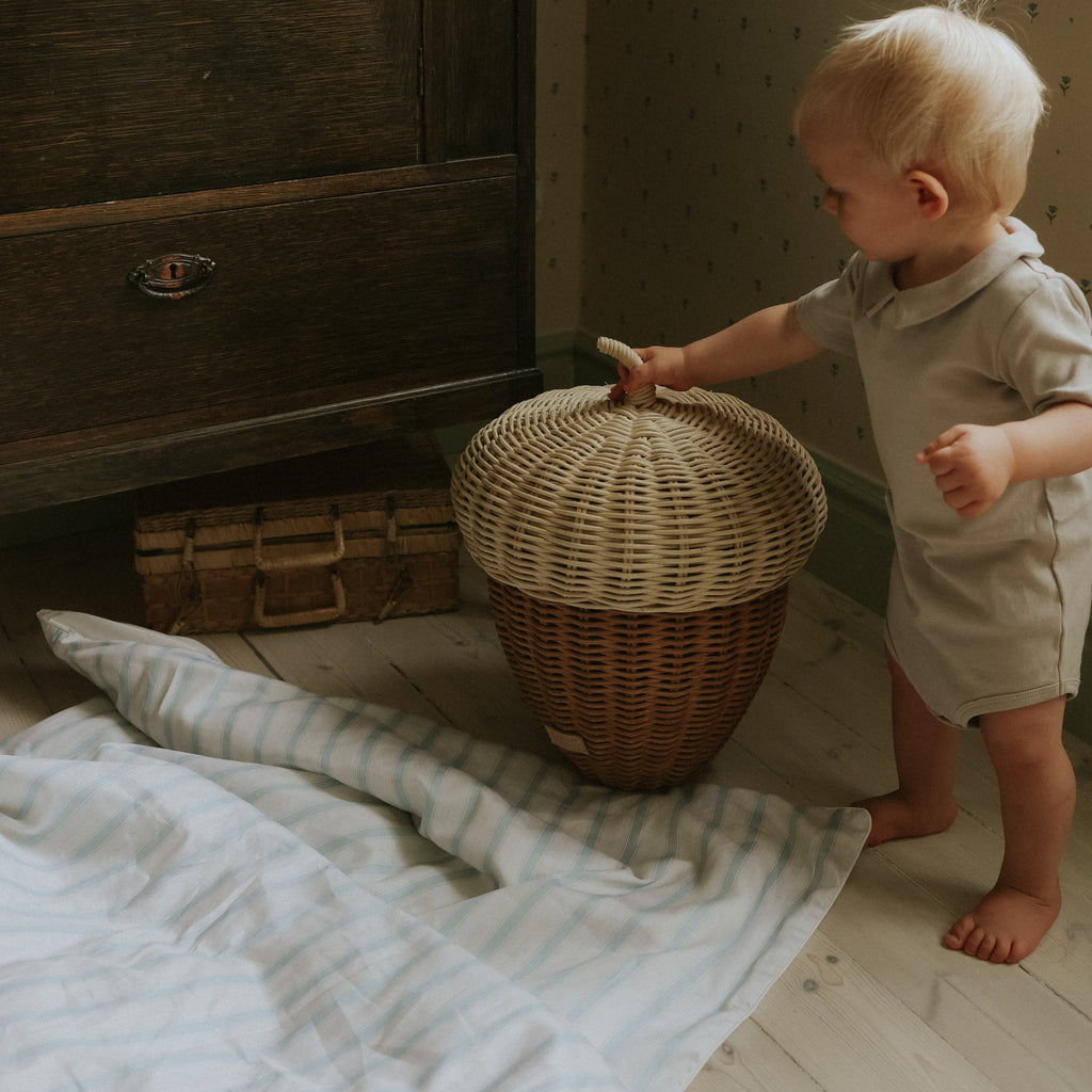 Toddler playing with mushroom bin with a toddler duvet on the floor in coastal stripes