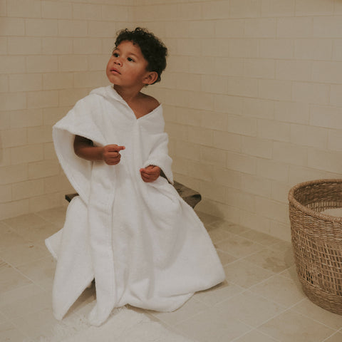 Toddler Poncho. Child sitting on a wooden stool with a rattan storage basket with towels sitting besides him