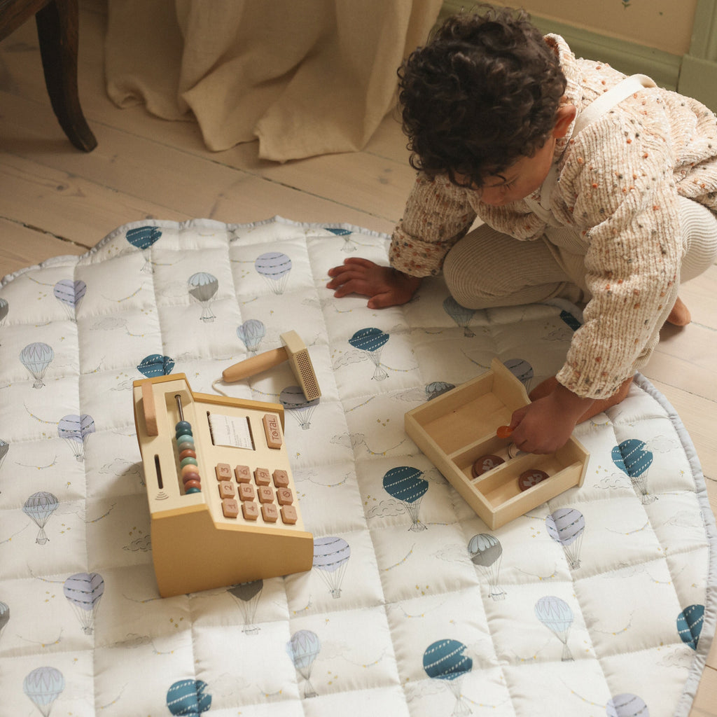 Touch the sky play mat in blue. Child is playing on play mat with wooden toy cash register