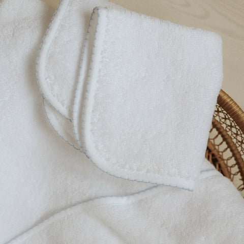 Classic washcloth in white with blue trim detail. Folded on top of bath towel