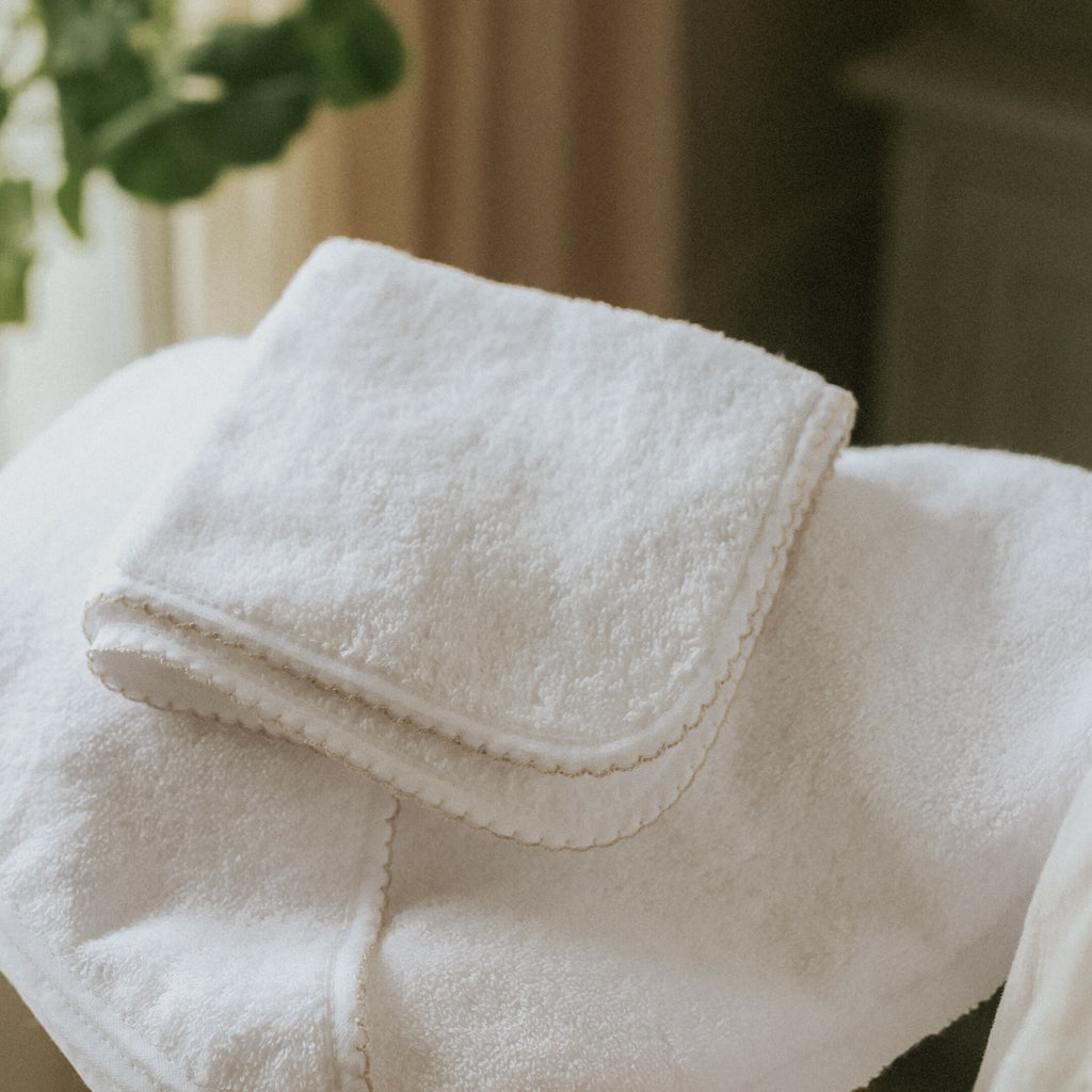 Classic washcloth in white with beige trim detail.  Folded on top of bath towel
