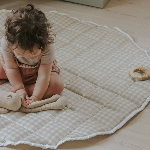 Picnic Gingham Play Mat in beige. Child is sitting on play mat playing with stuffed animail