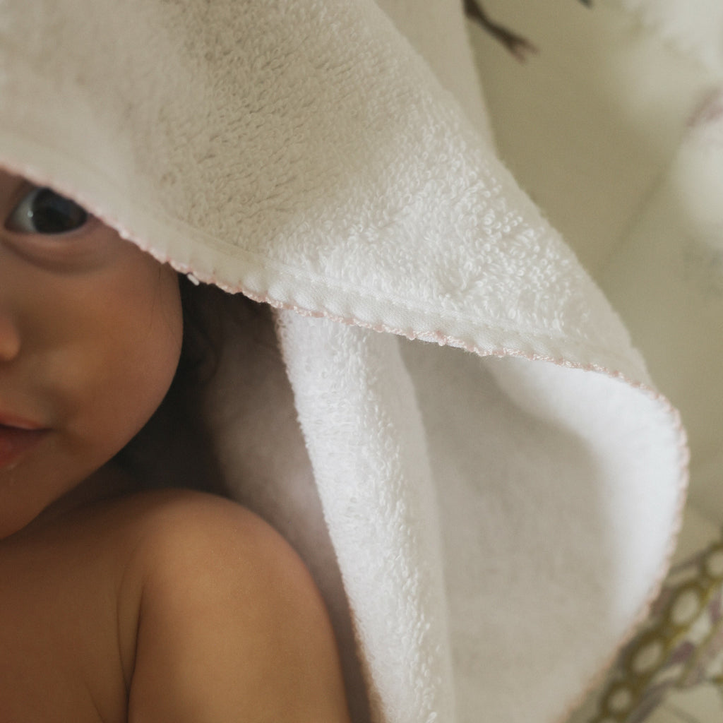Baby hooded towel in white with pink trim detail. Baby wearing hood 