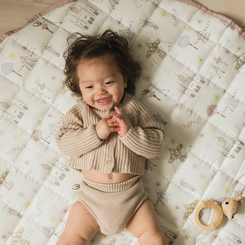 Adventure in Wonderland playmat in Rose. Child laying on her back smiling. Rattle next to her on playmat