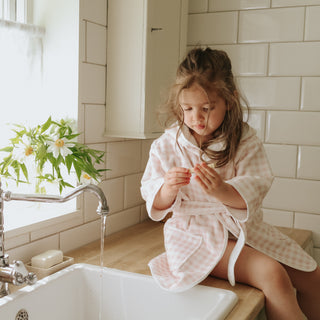 Child in a bathrobe sitting by a sink in a bathroom