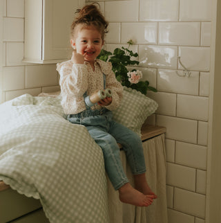 Picnic Gingham Green Toddler Duvet and Toddler Pillow on counter with little girl holding binoculars