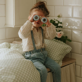Picnic Gingham Green Toddler Duvet and Toddler Pillow on counter with little girl holding binoculars