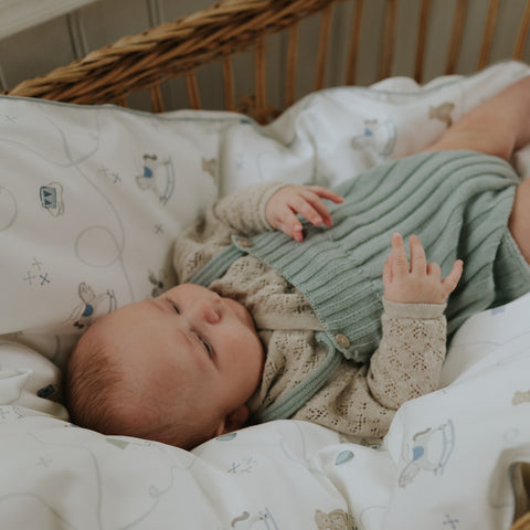 Baby lying in a crib wearing a green and beige outfit with a soft blanket.