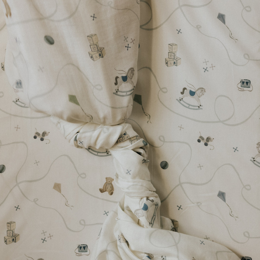 Baby swaddle on a crib sheet with toy prints on a crib