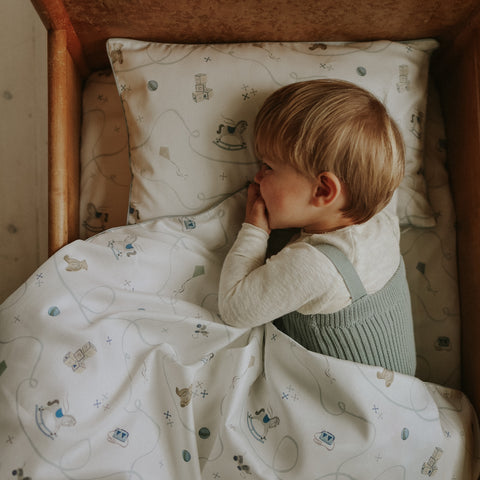 Child lying in a crib with patterned bedding and pillow