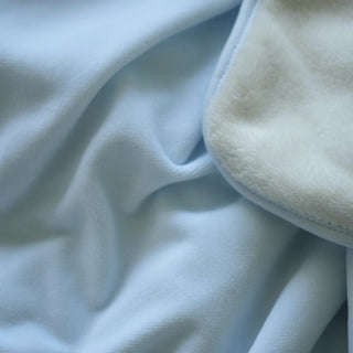 A close-up of a light blue fleece blanket with a soft, off-white sherpa lining visible along the folded edge.