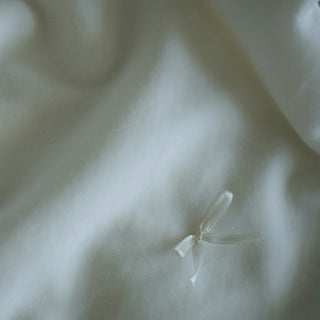 Close-up of soft white or off-white fabric with gentle folds and a small white ribbon tied near the upper right area.