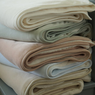 stack of cozy fleece blankets for baby in ivory, sage, blue, blush, pink