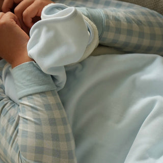 A close-up of a person wrapped in a light blue blanket, wearing a light blue and white gingham long-sleeve top.