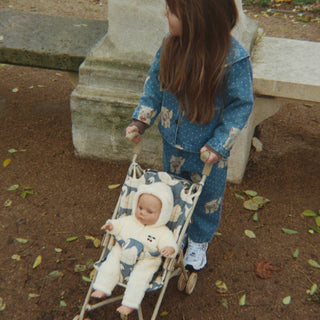 Child pushing a baby in a stroller outdoors on a leafy ground.