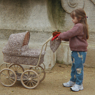 Little girl playing with a large scale leopard print doll pram. 