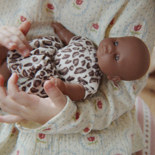 A close-up lifestyle shot of a person holding a baby doll dressed in a brown and white leopard print outfit.