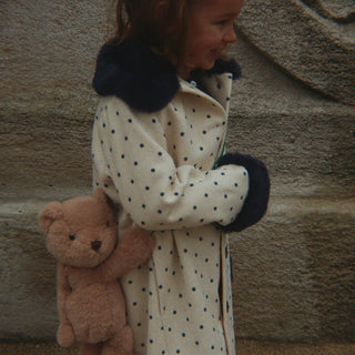 Little girl in a polka dot coat carrying a bear shaped purse.