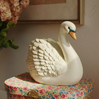 Decorative swan piggy bank on a floral-patterned box with a heart-patterned fabric background
