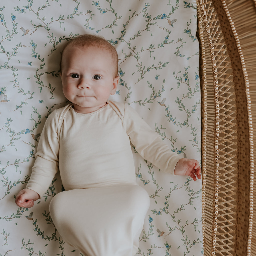 Baby laying on top of the "Secret Garden" printed crib sheet in the color ivory