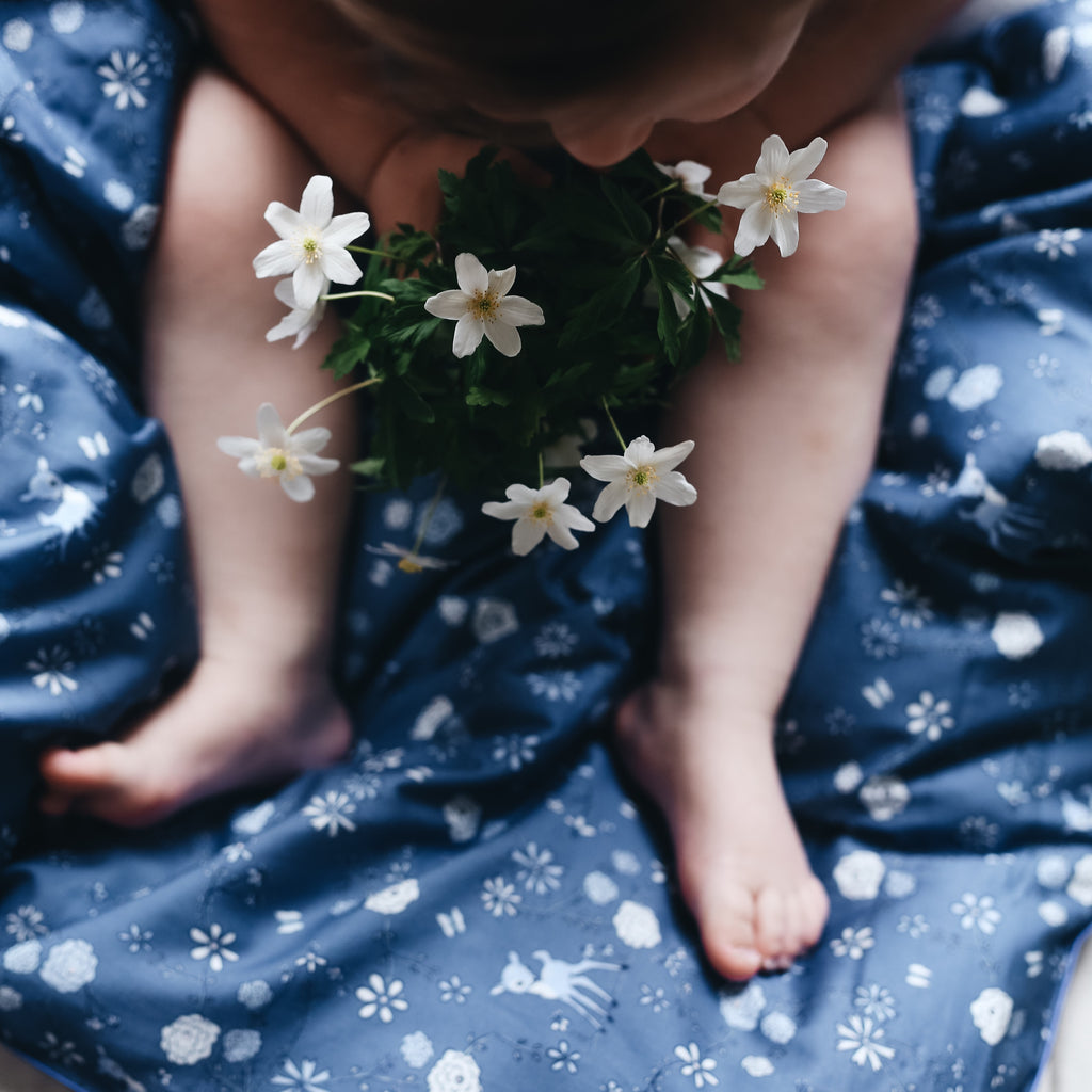 Toddler sitting on gooselings duvet holding flowers