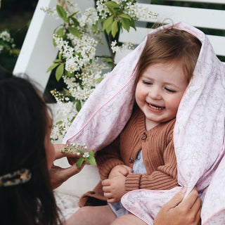 Toddler playing peek a boo with mother, with gooselings duvet in the print "Bird's Song" in the color pink