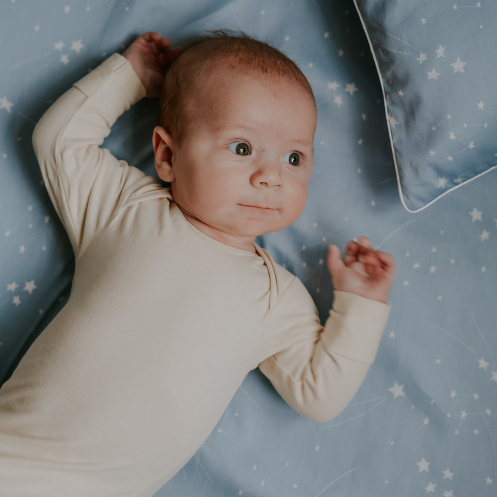 Baby laying on top of crib sheet in the print "Once Upon A Time" in the color blue